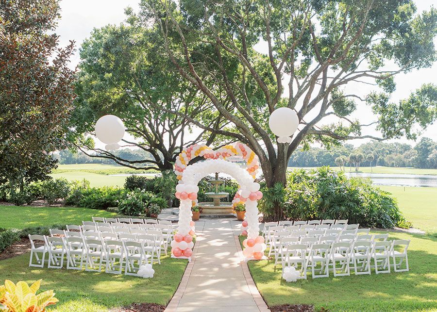 A wedding ceremony is being held in a park with balloons and chairs.