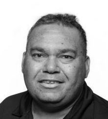 A man in a black shirt is smiling in a black and white photo.