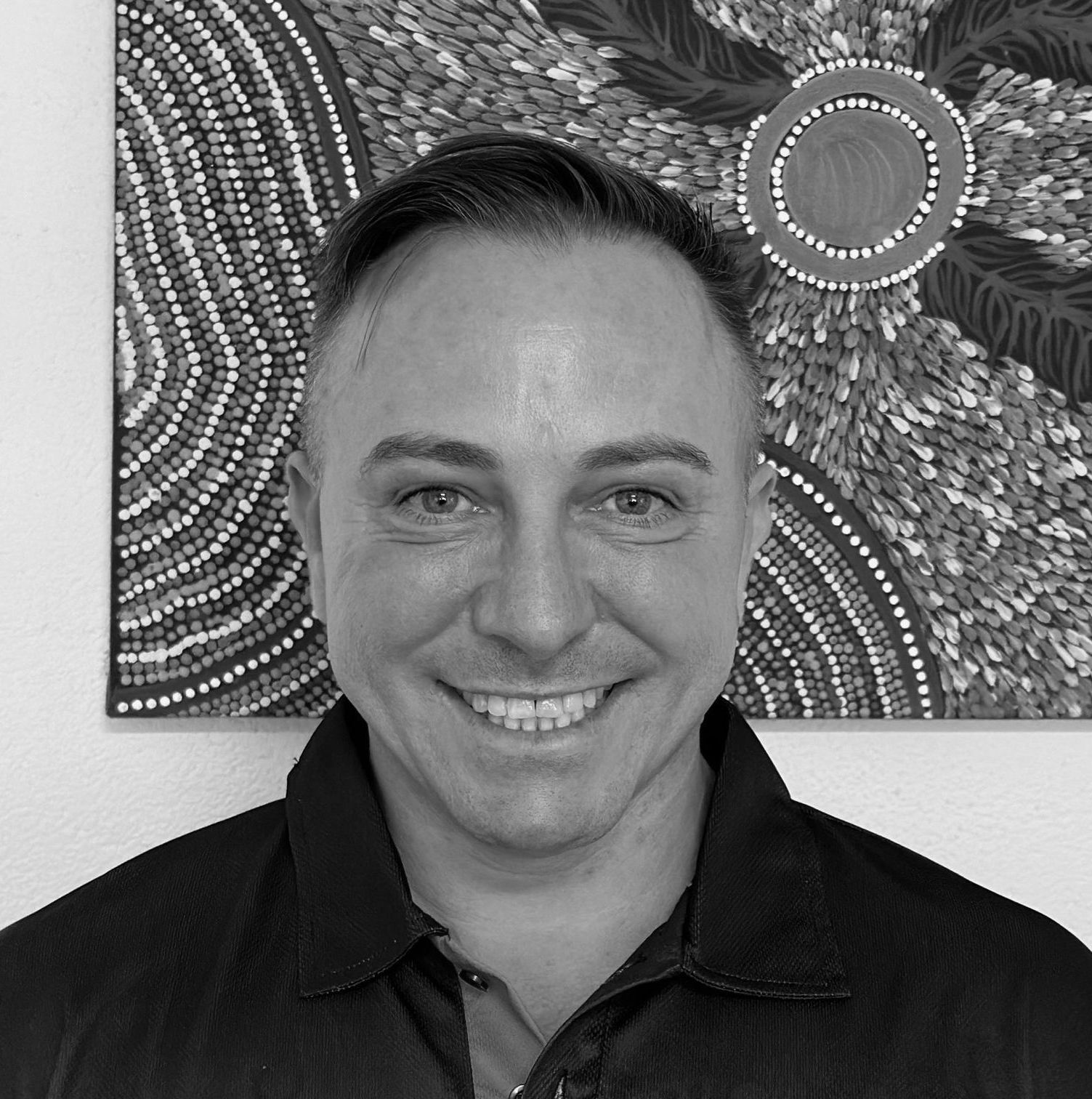 A man is smiling in front of a painting on a wall.