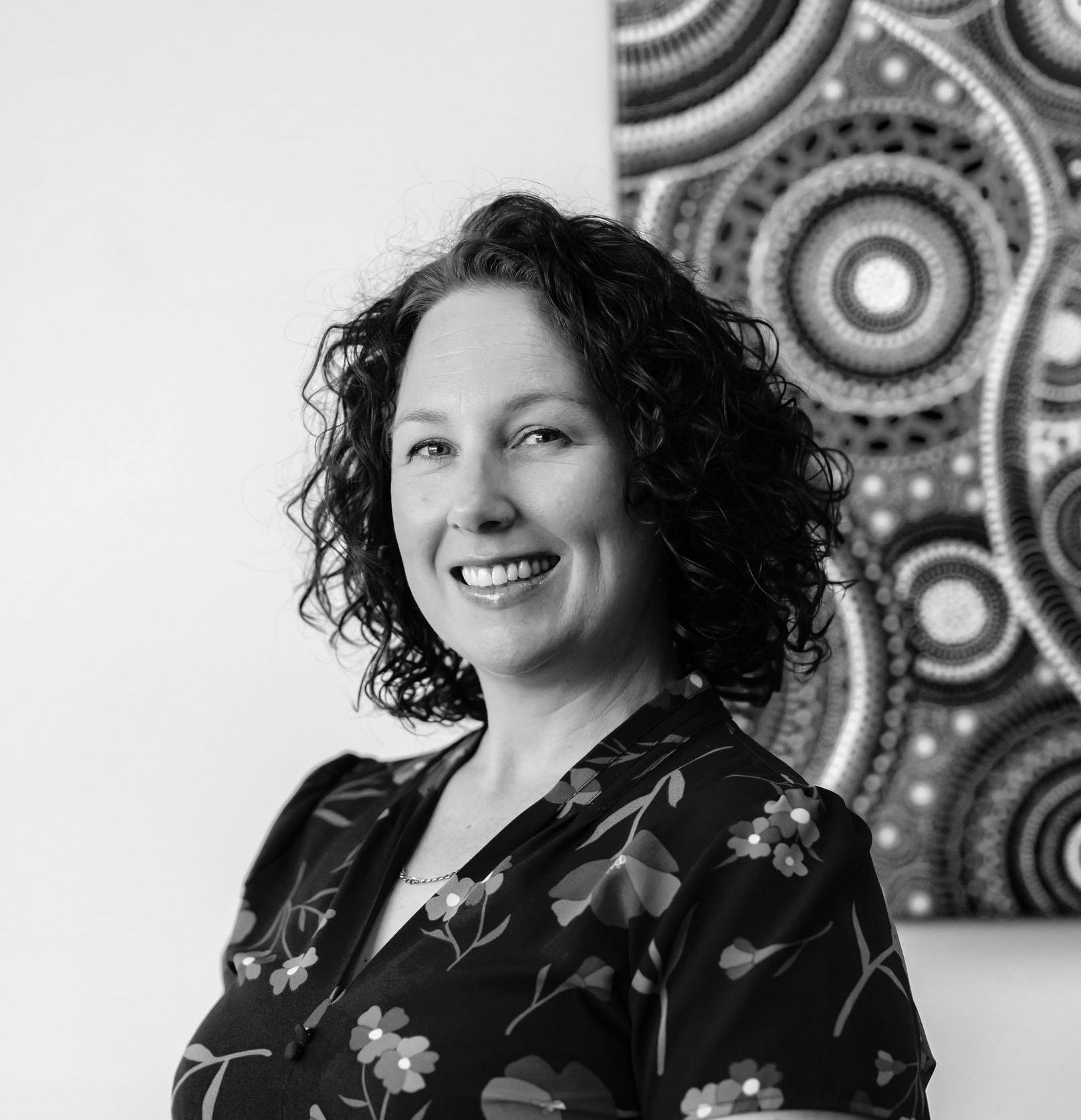 A woman is smiling in front of a painting on the wall.