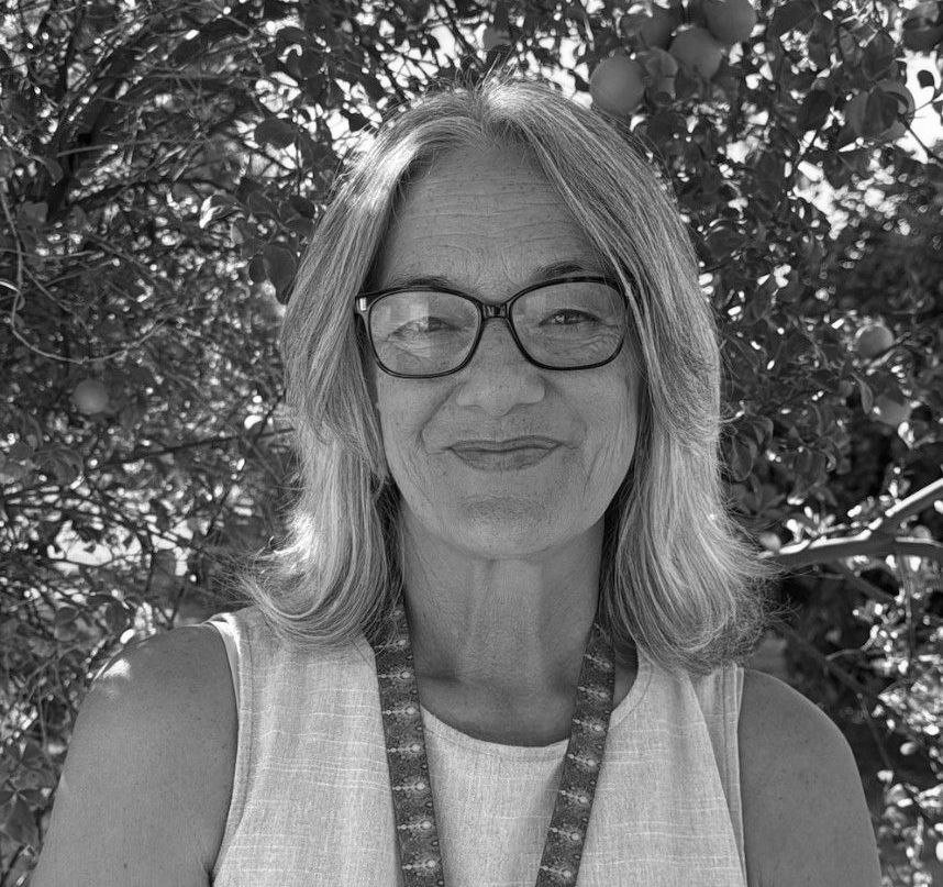 A woman wearing glasses is standing in front of a tree in a black and white photo.