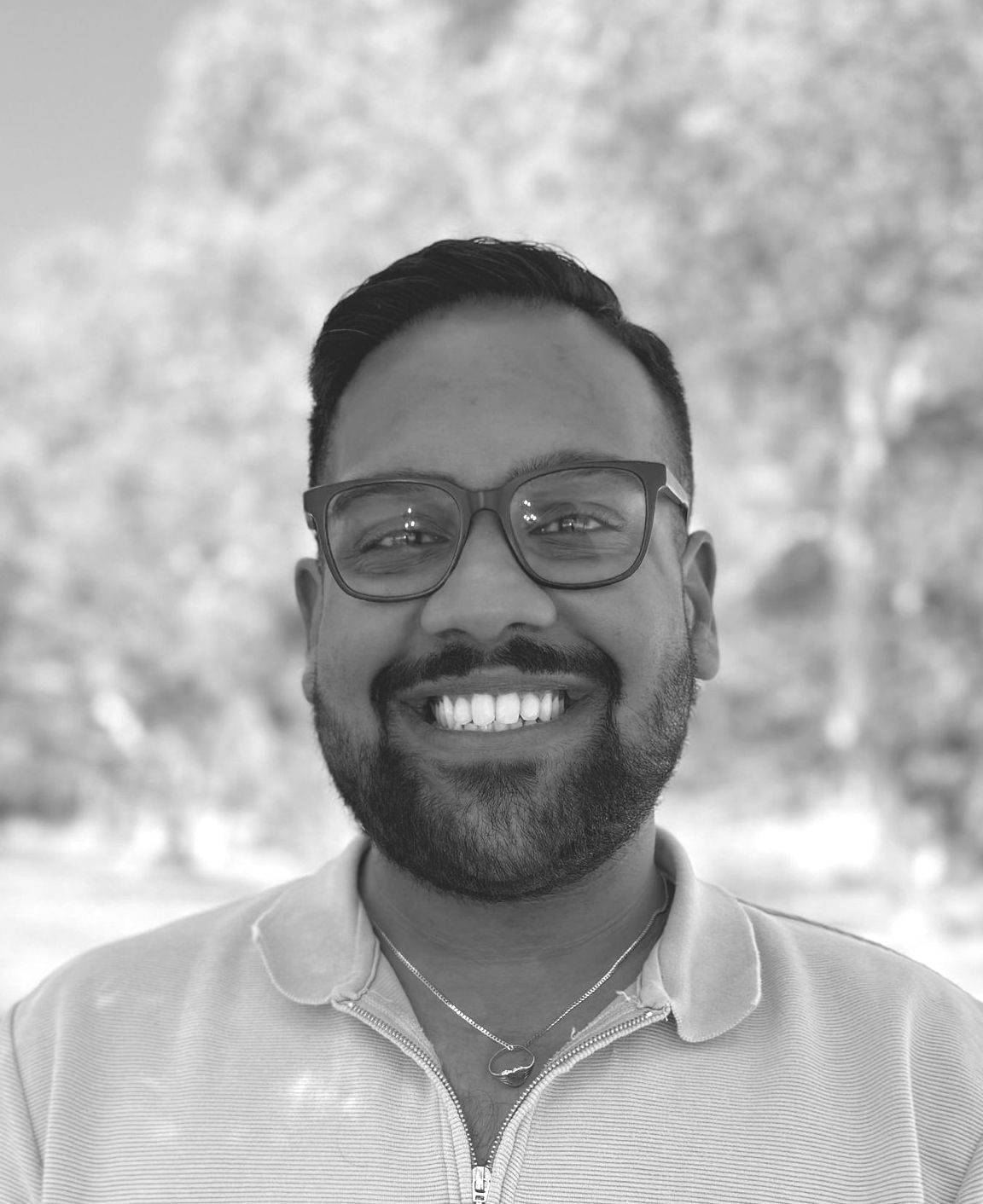 A man with a beard and glasses is smiling in a black and white photo.