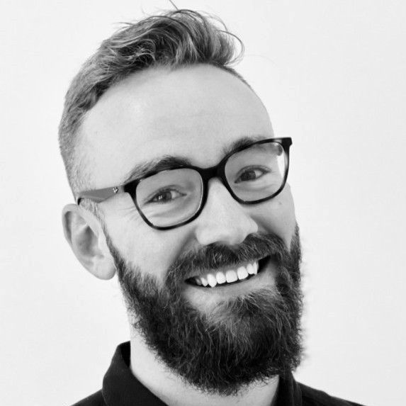 A man with a beard and glasses is smiling in a black and white photo.