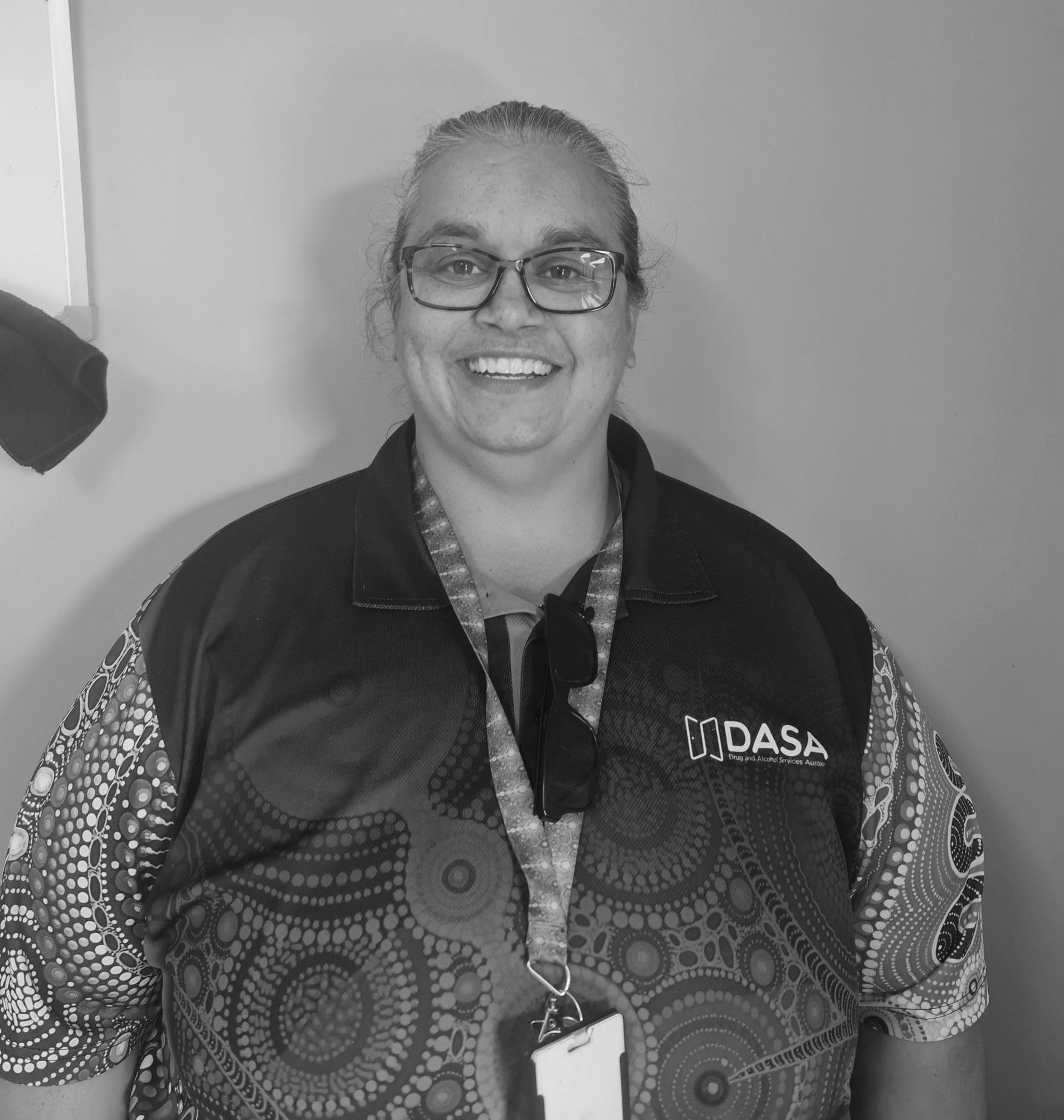 A woman wearing glasses and a dasa vest is smiling in a black and white photo.