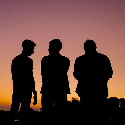Silhouettes of three people standing in front of a sunset