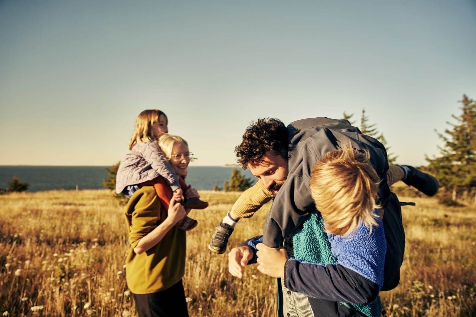 A man is carrying two children on his shoulders in a field.