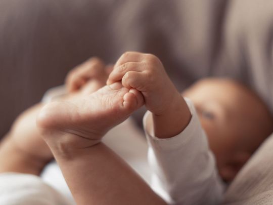 Un bébé est allongé sur un canapé et tient son pied.