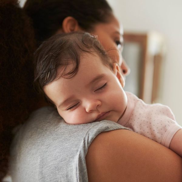 Une femme tient un bébé qui dort sur son épaule.