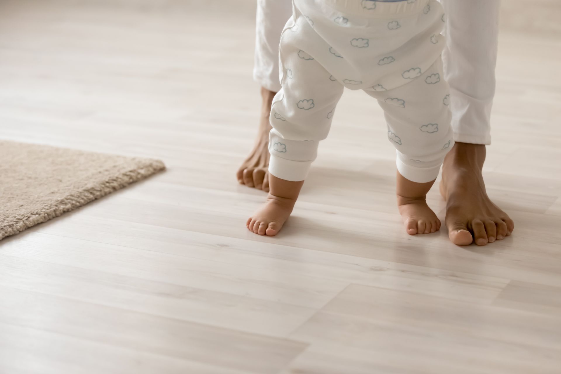 A baby is walking barefoot on a wooden floor.