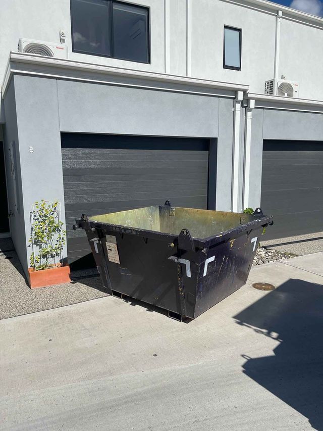 A dumpster is sitting on the sidewalk in front of a building.