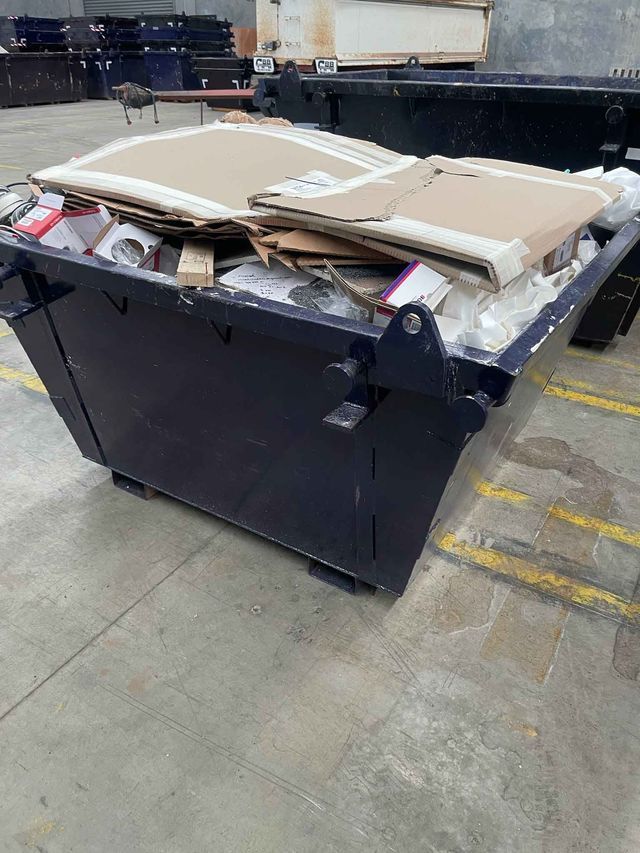 A dumpster filled with cardboard boxes is sitting on the ground in a warehouse.