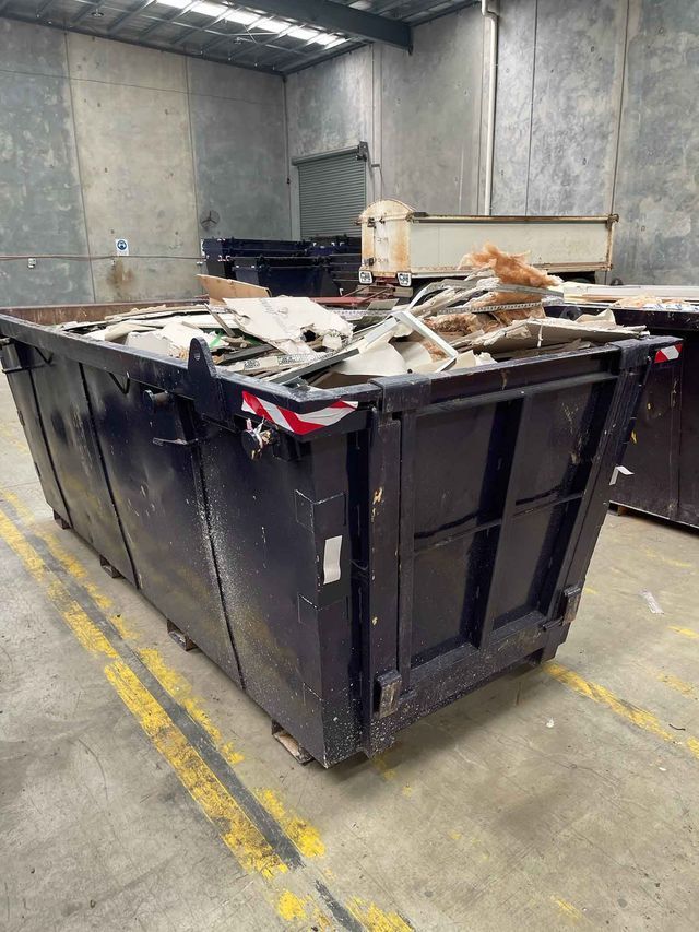 A large black dumpster filled with junk is sitting in a warehouse.