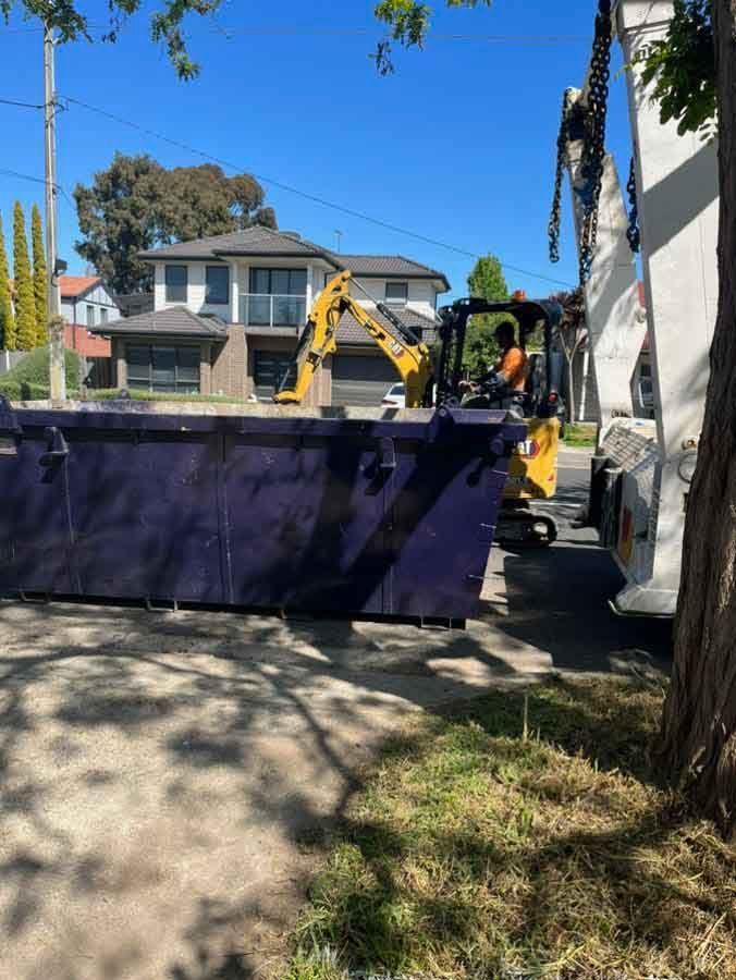 A dumpster is being loaded onto a truck by a yellow excavator.