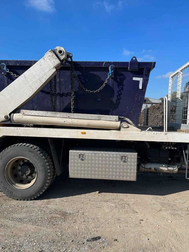 A dump truck is parked in a dirt lot with a blue sky in the background.