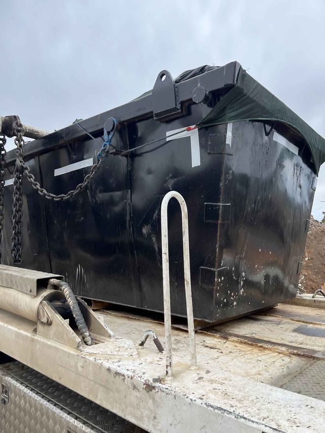 A large black dumpster is sitting on top of a truck.