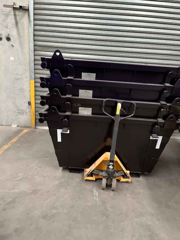 A pallet truck is pushing a stack of dumpsters in a warehouse.