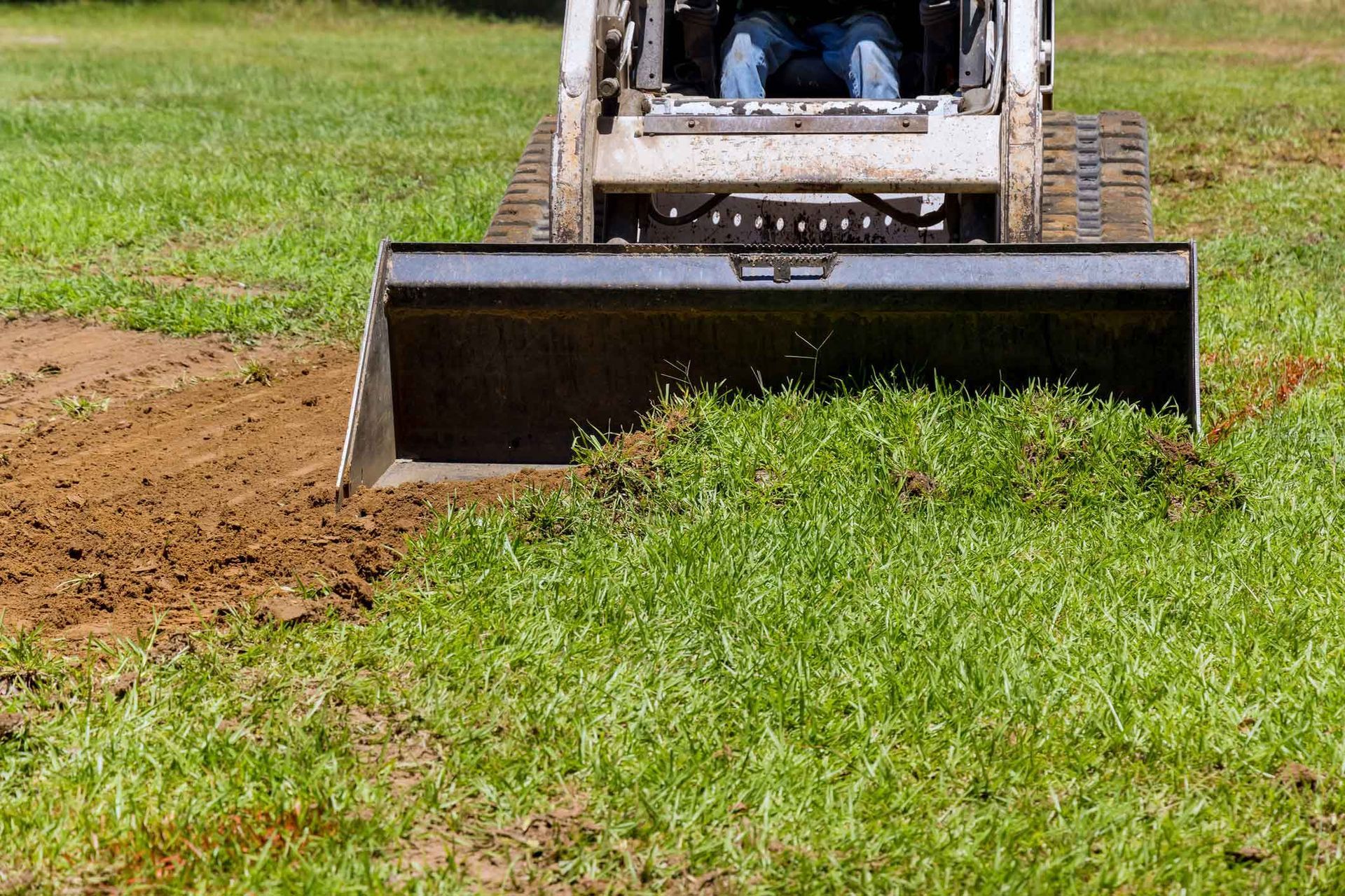 Skid steer removing grass and dirt from a lawn.