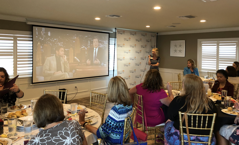A group of women are sitting at tables watching a presentation on a large screen.