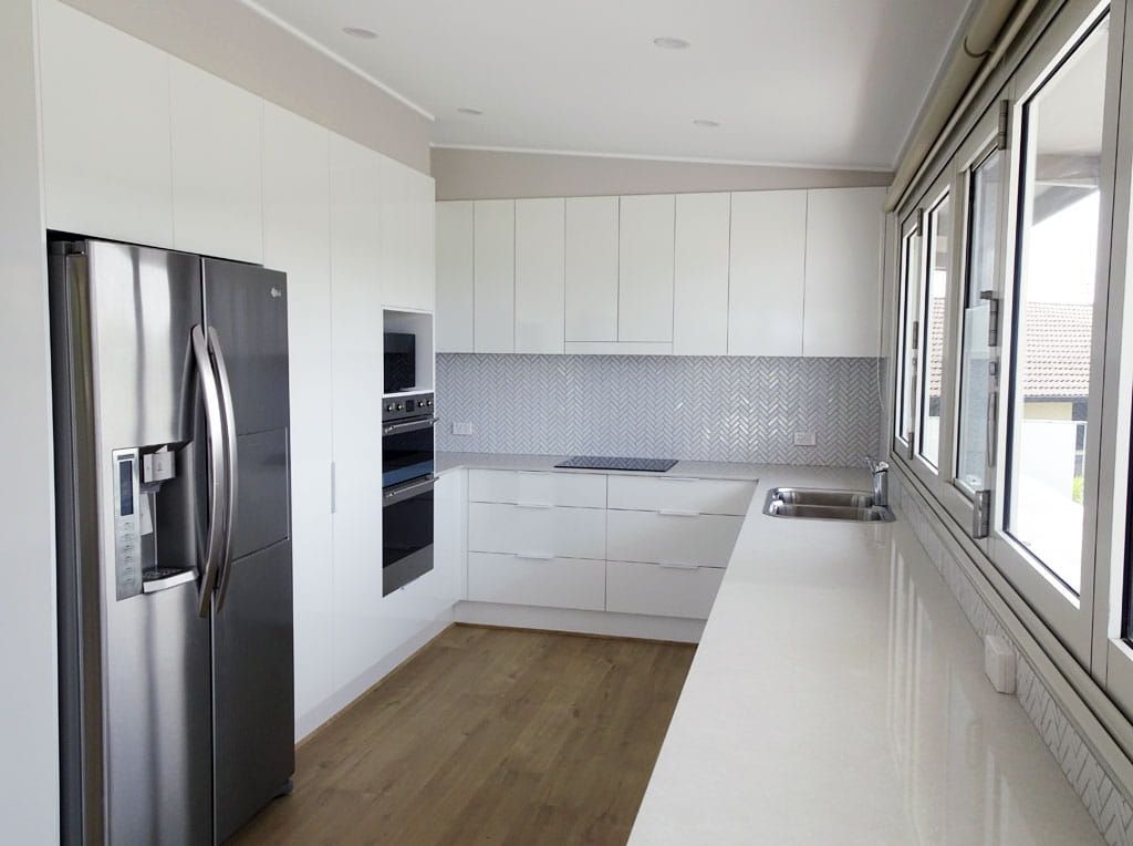 A Kitchen With White Cabinets, A Refrigerator And A Sink — Beach Breeze Building In Tumbi Umbi, NSW