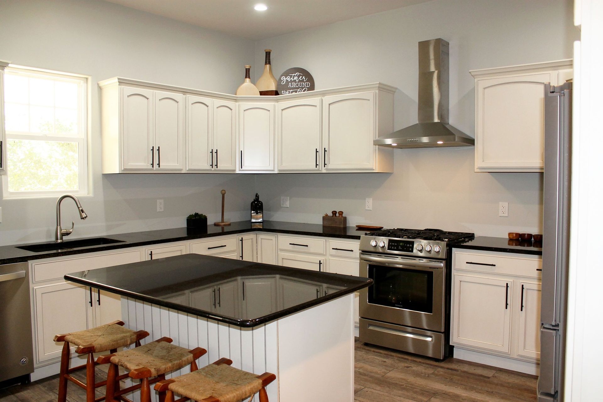 A kitchen with white cabinets , black counter tops , stainless steel appliances and a large island.