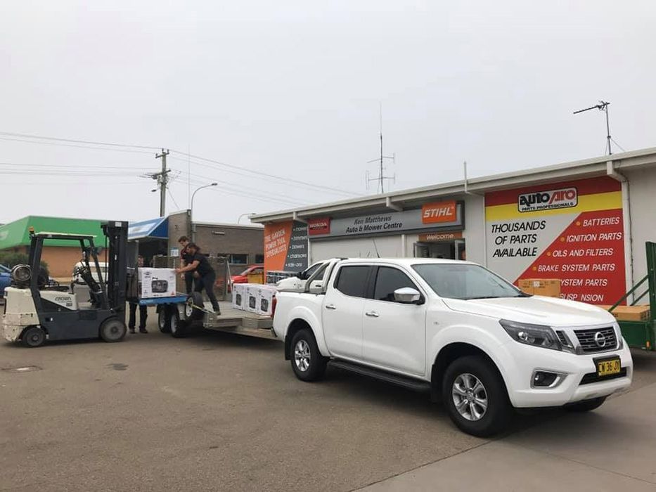 A White Truck Is Being Towed By A Forklift In Front Of A Building — Ken Matthews Auto & Mower Centre In Ulladulla, NSW