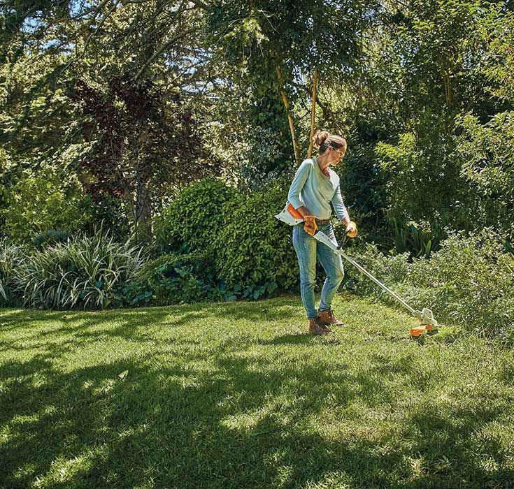 A Woman Is Using A Lawn Mower To Cut The Grass — Ken Matthews Auto & Mower Centre In Ulladulla, NSW