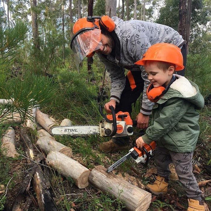 A Man And A Boy Are Cutting Logs With A Chainsaw — Ken Matthews Auto & Mower Centre In Ulladulla, NSW