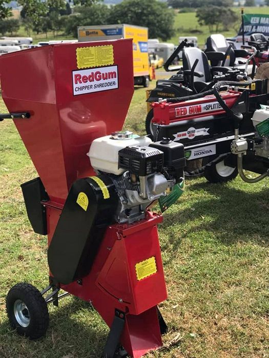 A Red Chipper Is Sitting In The Grass Next To A Tractor — Ken Matthews Auto & Mower Centre In Ulladulla, NSW