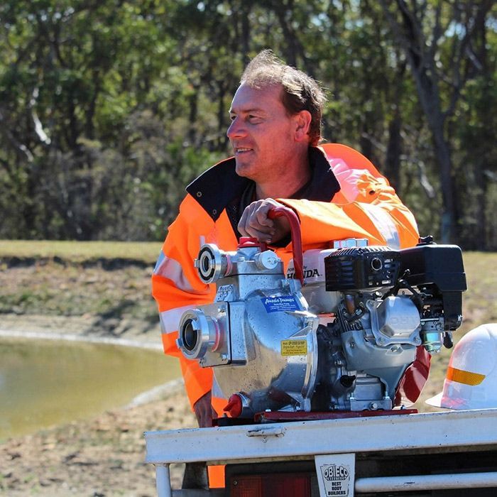 A Man In An Orange Jacket Is Holding A Water Pump — Ken Matthews Auto & Mower Centre In Ulladulla, NSW