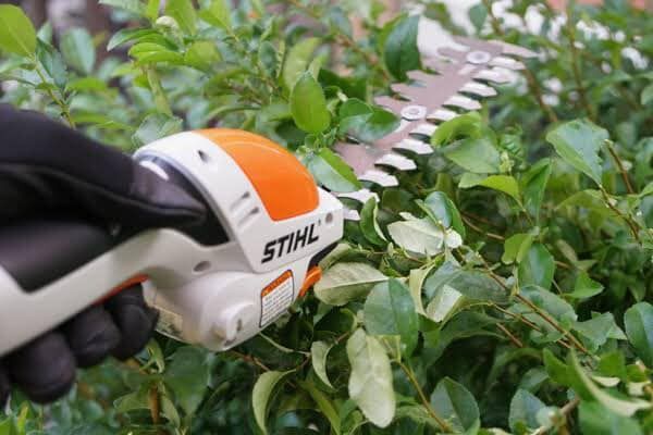 A Person Is Using A STIHL Hedge Trimmer To Cut A Bush — Ken Matthews Auto & Mower Centre In Ulladulla, NSW