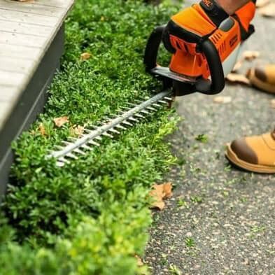 A Person Is Cutting A Hedge With A Hedge Trimmer — Ken Matthews Auto & Mower Centre In Ulladulla, NSW