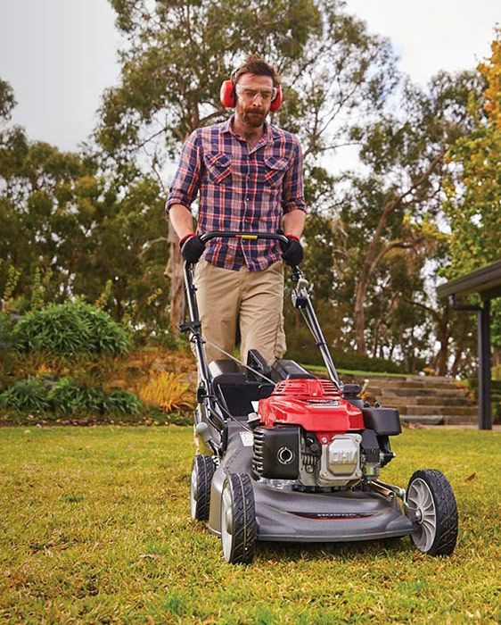 A Man Is Using A Lawn Mower On A Lush Green Lawn — Ken Matthews Auto & Mower Centre In Ulladulla, NSW