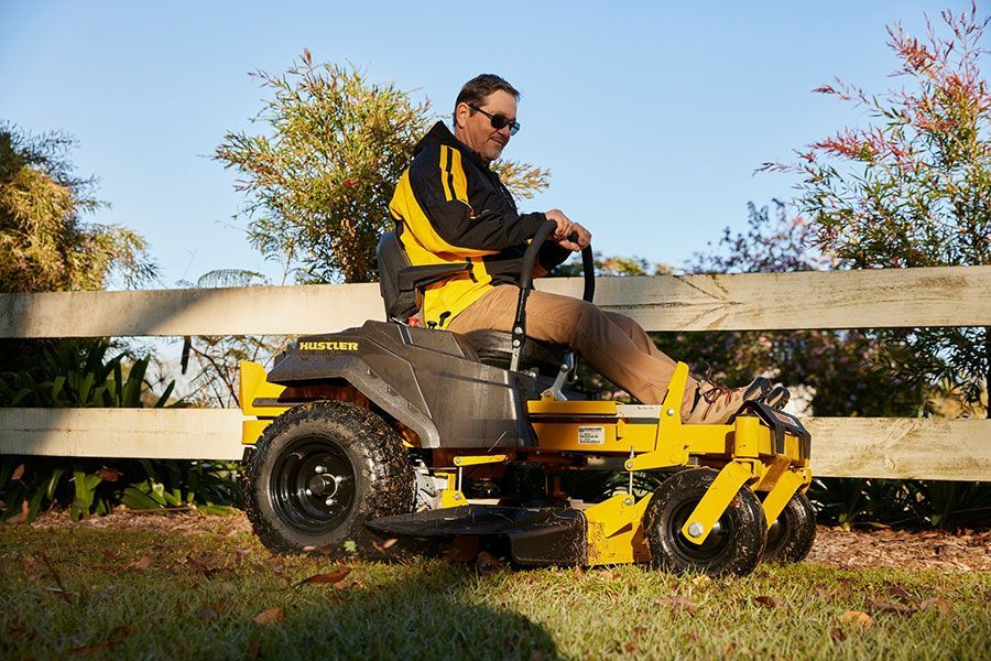 A Man Is Riding A Yellow Lawn Mower Next To A Wooden Fence — Ken Matthews Auto & Mower Centre In Ulladulla, NSW