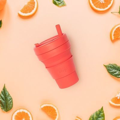 A red cup with a straw is surrounded by oranges and leaves