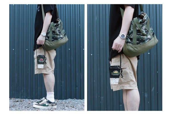 A man wearing shorts and a black shirt is holding a green bag.