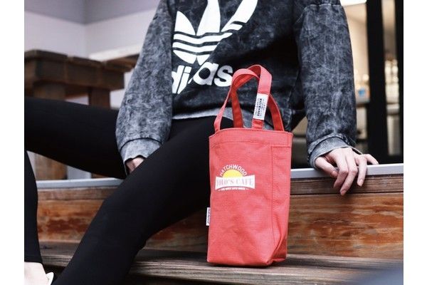 A person is sitting on a bench holding a red tote bag.