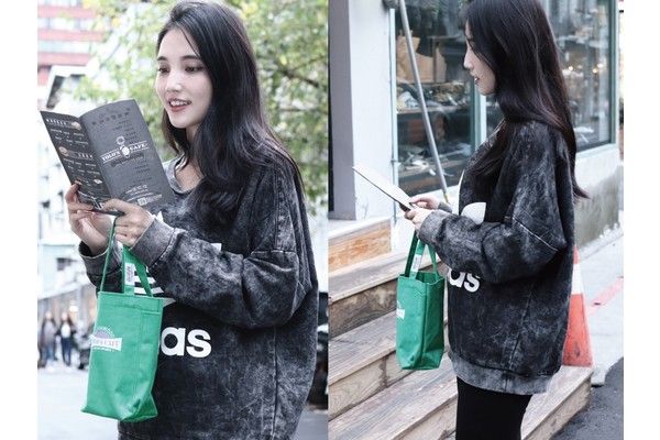 A woman is holding a green tote bag and reading a book.