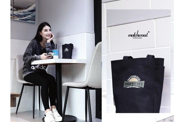 A woman is sitting at a table with a tote bag next to her.