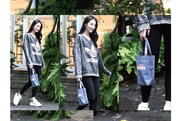 A woman in an adidas sweatshirt is holding a blue tote bag.