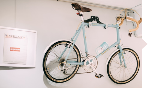 A bicycle is hanging on a wall next to a supreme poster.