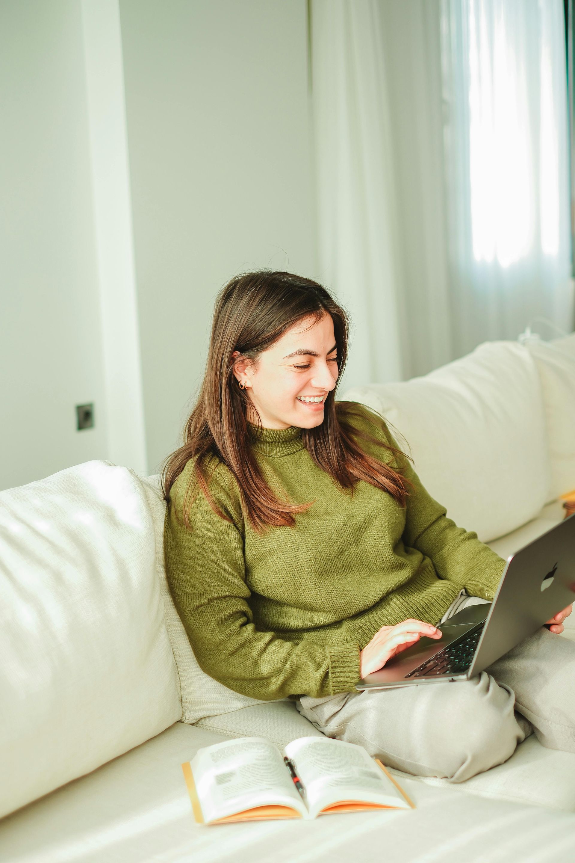 A woman is sitting on a couch using a laptop computer.