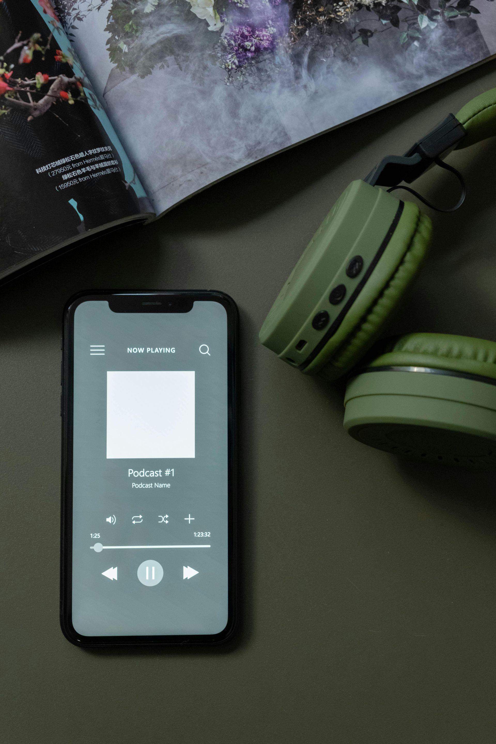 A cell phone and headphones are sitting on a table next to a magazine.