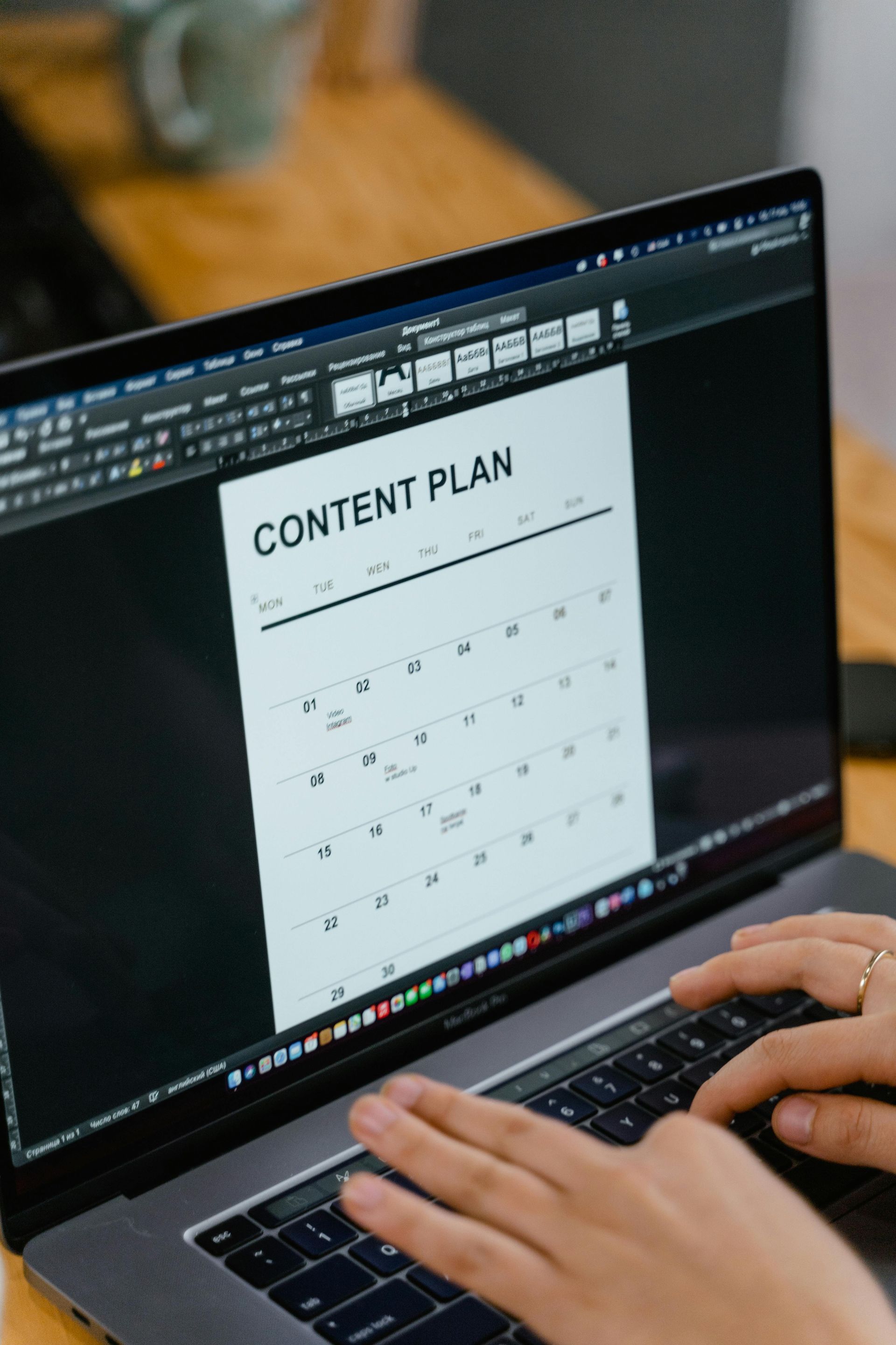 A person is typing on a laptop with a content plan on the screen.