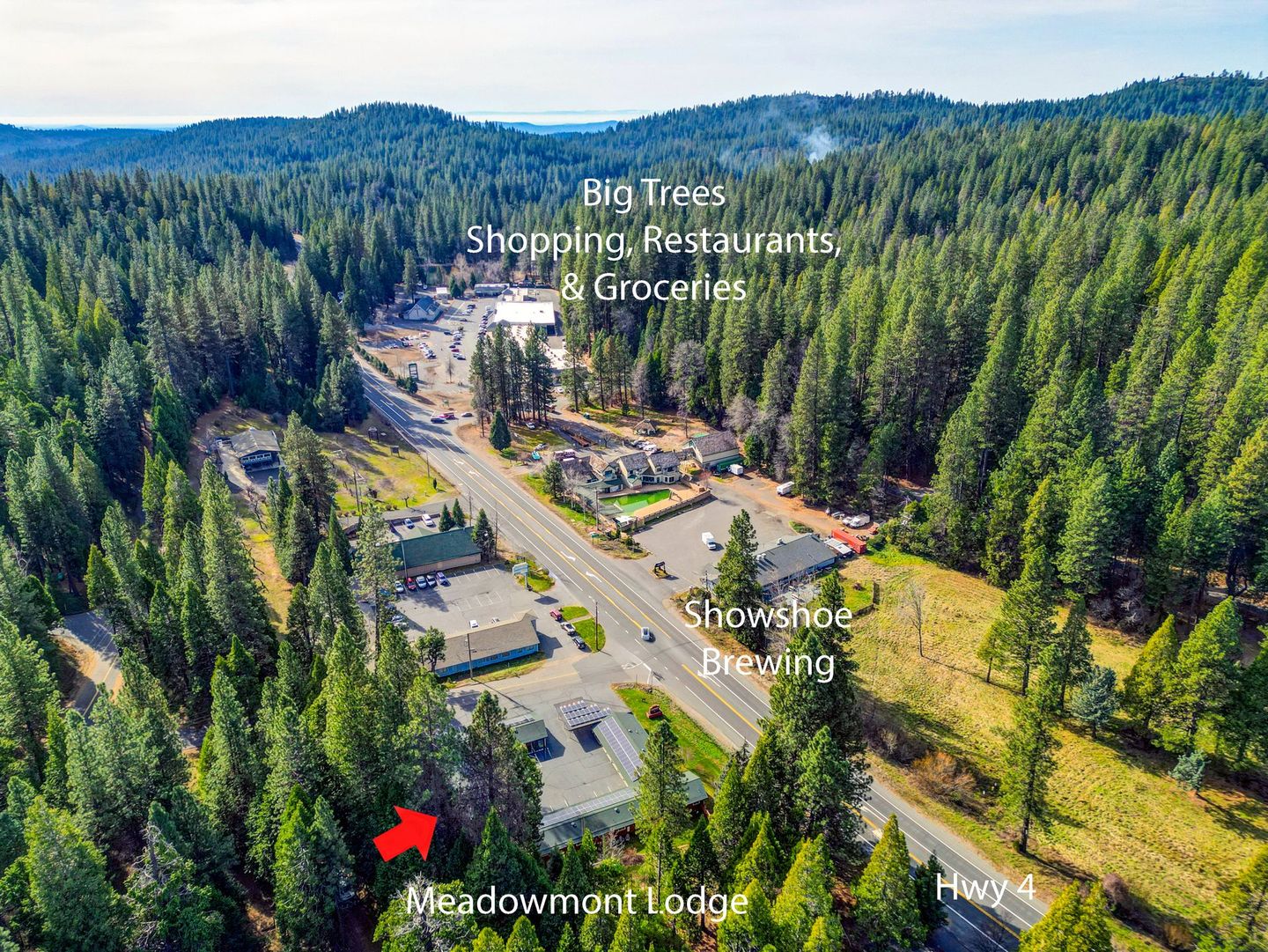 Aerial view of Meadowmont Lodge and nearby businesses along Hwy 4, surrounded by a dense forest.