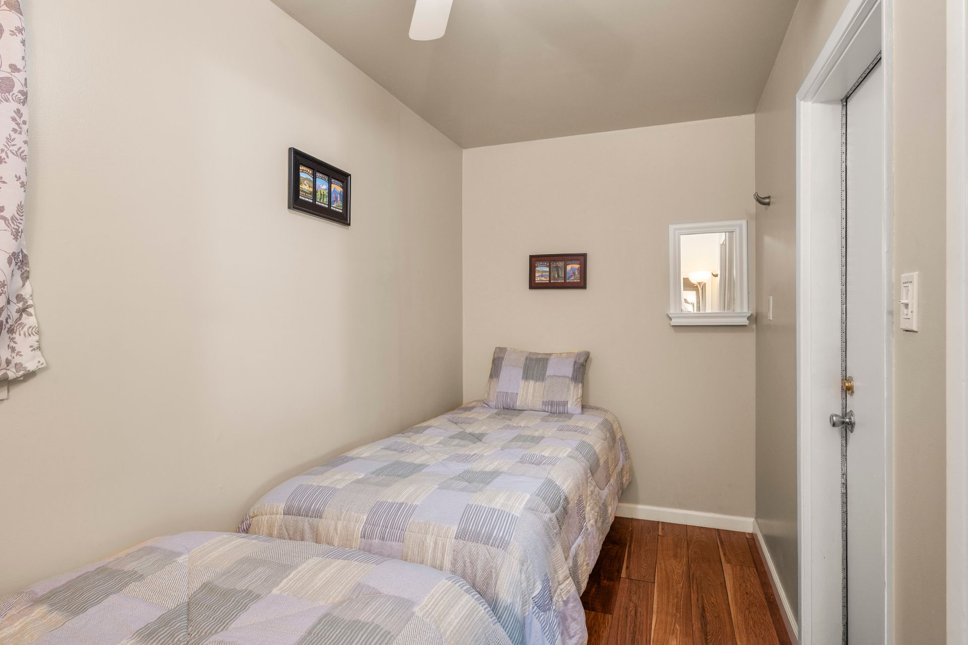 A small bedroom with two single beds featuring patterned blue-and-white quilts, beige walls, and light wood flooring.