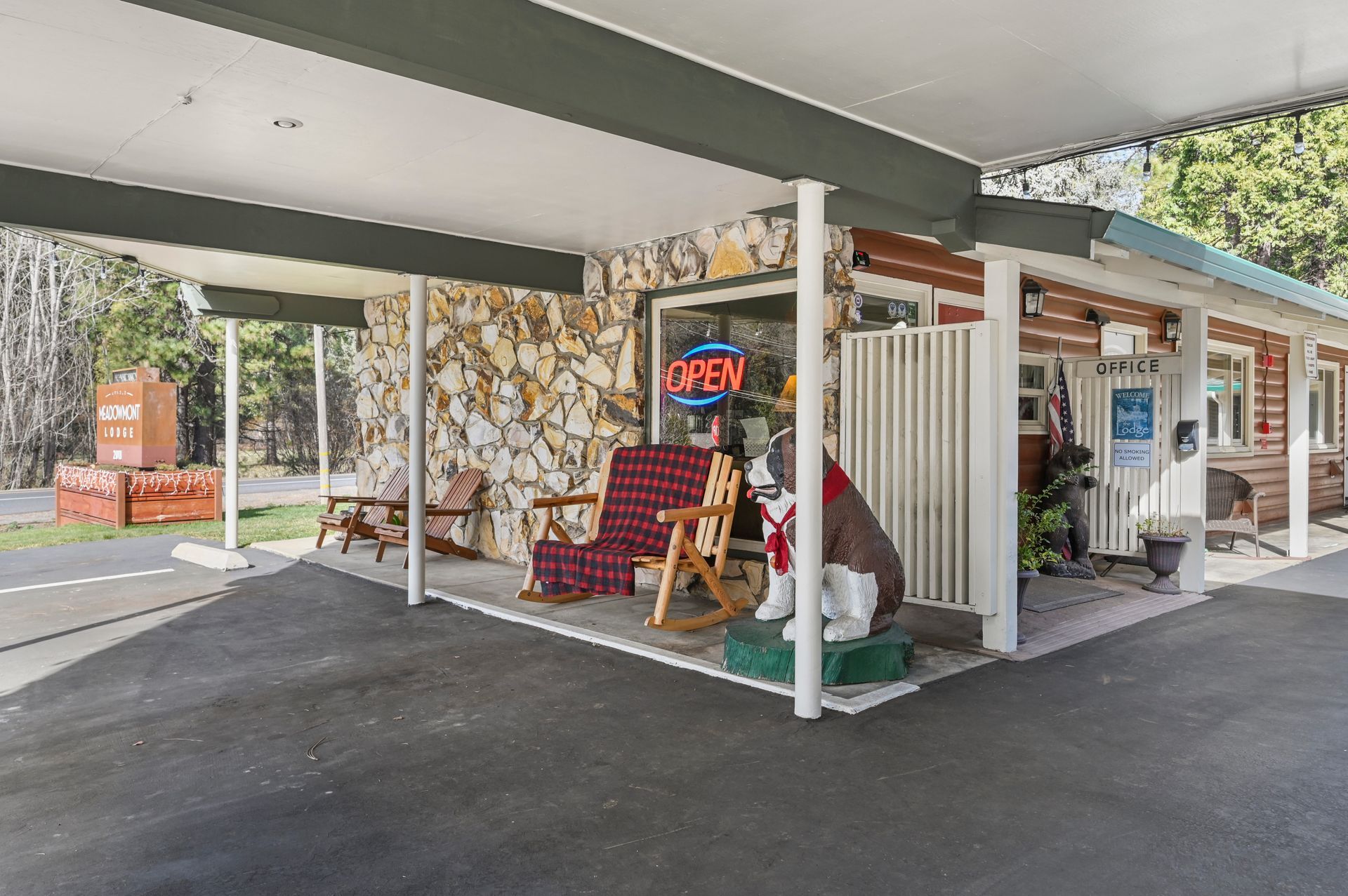 Covered motel walkway with vending machines, red chairs, and a neon “OPEN” sign outside rooms