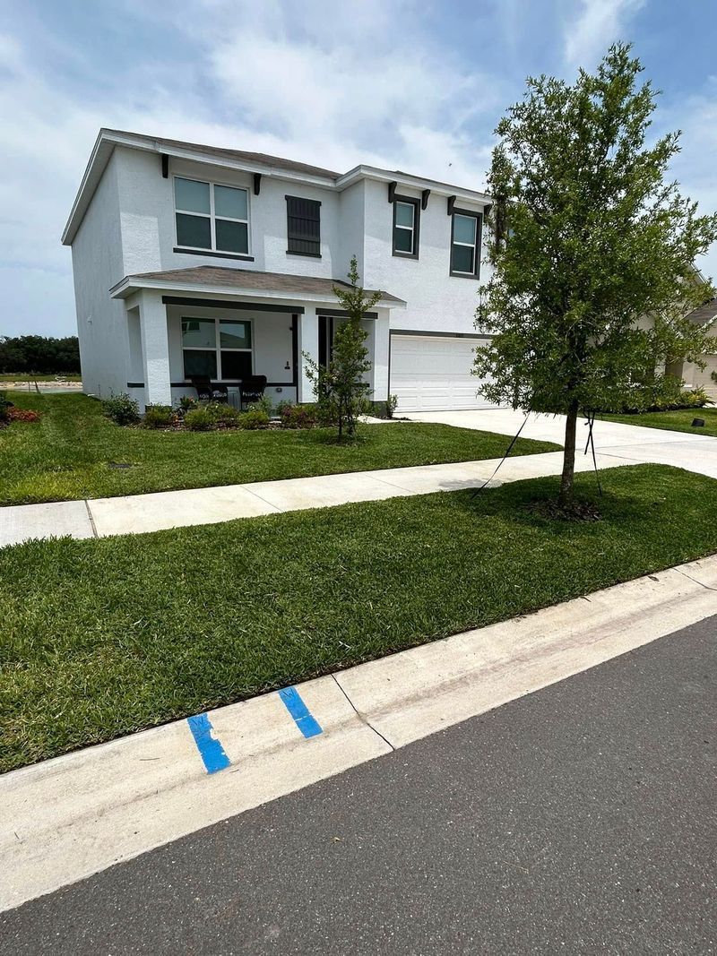 Two-story white house with green grass and a tree, seen from the street. 
