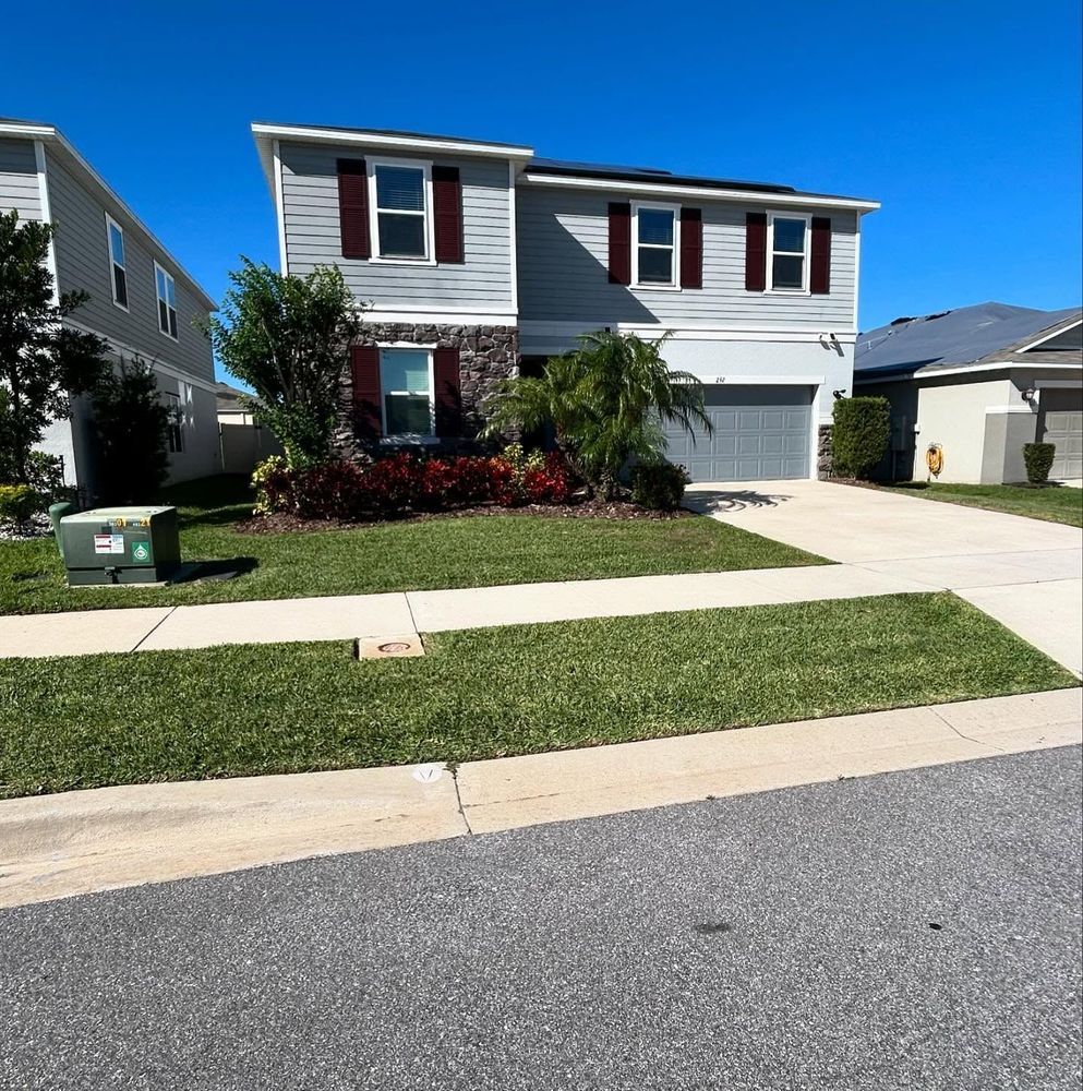 Two-story house with gray siding, red shutters, and a green lawn under a clear blue sky.
