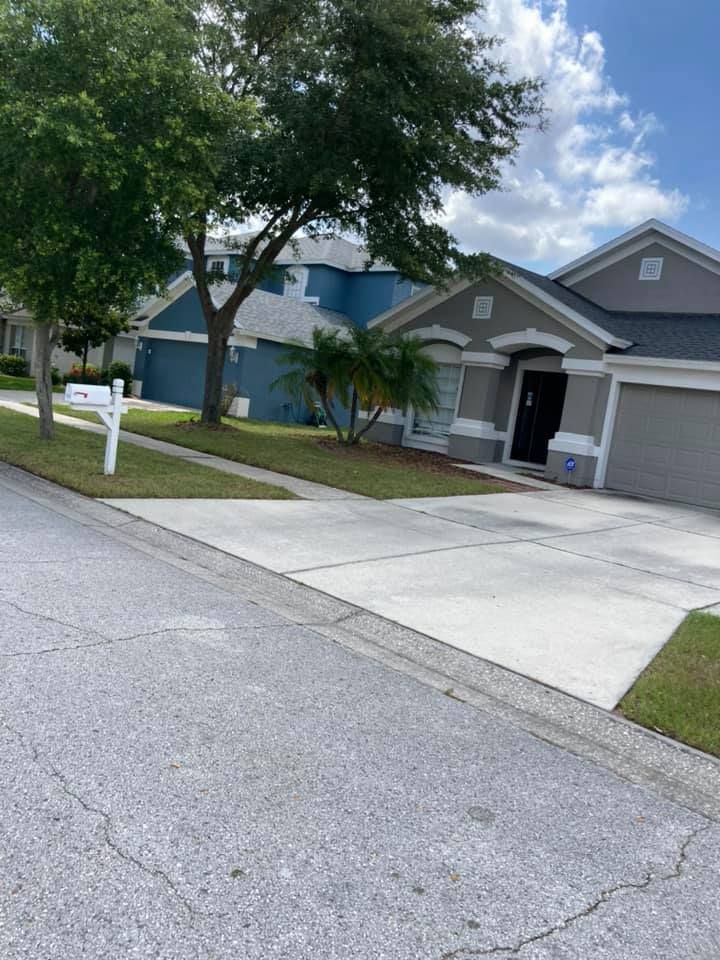 Suburban homes with driveways, green lawns, and trees, under a cloudy sky.