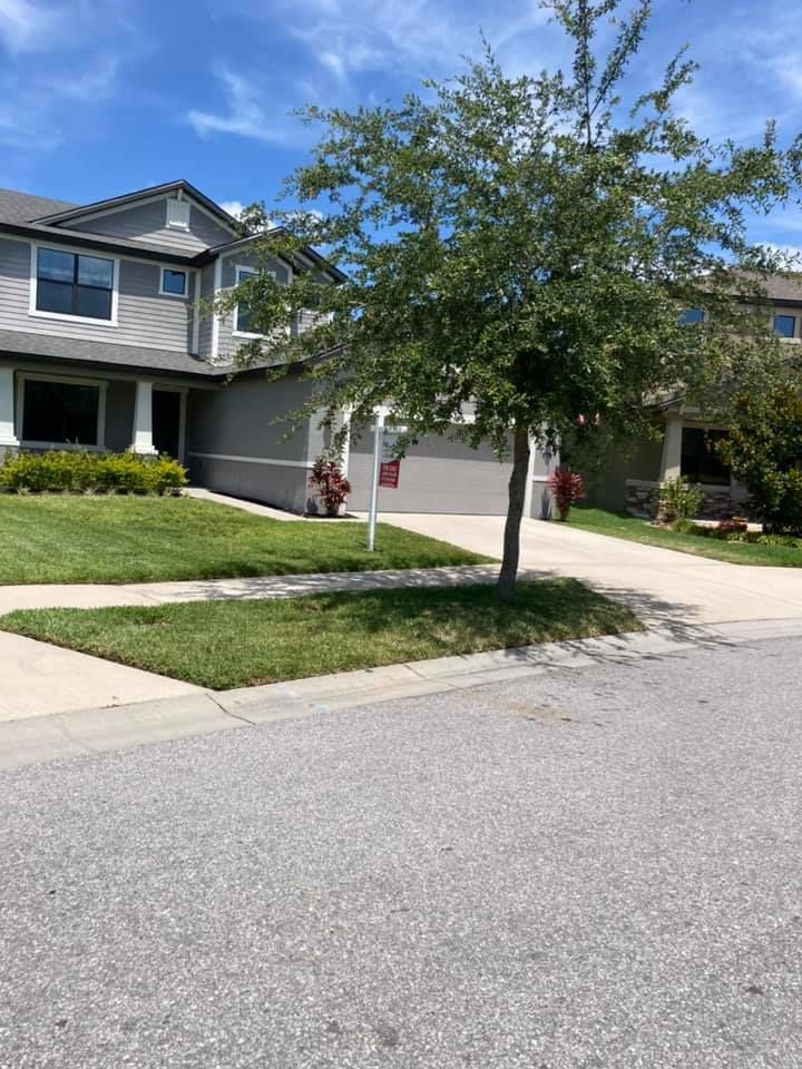 Two-story gray house with garage, green lawn, tree in front, sunny day.